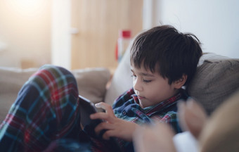 快乐孩子与微笑脸有有趣的玩游戏在线平板电脑与朋友圣诞节假期孩子男孩穿圣诞节睡衣放松首页的早....