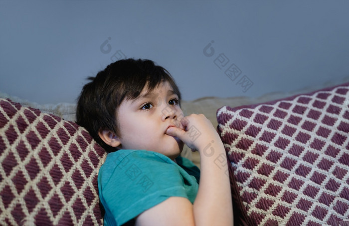 肖像孩子说谎萨法咬他的手指指甲而看小男孩坐着沙发上咬他的指甲孩子令人心寒的出放松生活房间周末