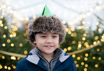 快乐可爱的男孩与微笑脸穿聚会，派对他对模糊灯圣诞节树孩子有有趣的传统的庆祝活动圣诞节市场孩子站照亮圣诞节树