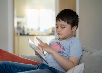 孩子坐着沙发看卡通玩游戏平板电脑孩子男孩使用数字垫学习教训在线互联网首页学校教育距离学习在线教育凹陷