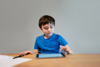 学校孩子学习在线类房间首页孩子使用平板电脑为家庭作业年轻的男孩研究在线视频调用电子学习在家教育教育概念