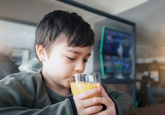 肖像年轻的孩子喝新鲜的橙色汁为早餐咖啡馆快乐孩子男孩喝玻璃水果汁而等待为食物餐厅健康的食物生活方式概念