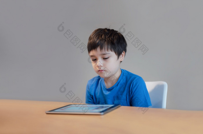 学校孩子使用平板电脑做在线家庭作业孩子与无聊脸阅读书数字读者年轻的男孩阅读故事电子书首页学校教育学习在线教育概念