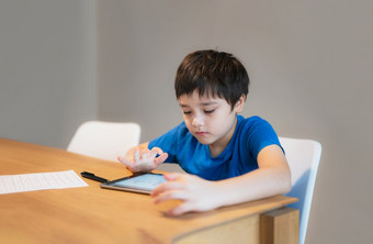 学校孩子学习在线类房间首页孩子使用平板电脑为家庭作业年轻的男孩研究在线视频调用电子学习在家教育教育概念