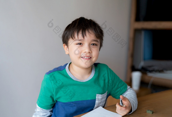 快乐男孩使用铅笔画草图纸可爱的孩子看相机与微笑脸选址表格做家庭作业孩子享受艺术和工艺活动首页教育概念