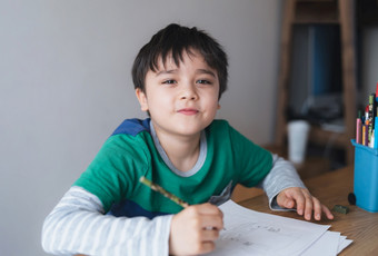 快乐男孩使用铅笔画草图纸可爱的孩子看相机与微笑脸选址表格做家庭作业孩子享受艺术和工艺<strong>活动首页</strong>教育概念