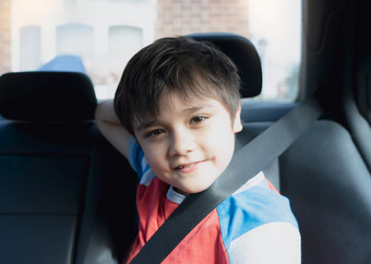 肖像快乐年轻的男孩选址安全车座位看相机与微笑脸孩子坐着的回来乘客座位与安全带学校孩子旅行学校车回来学校