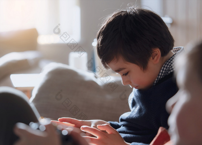 电影肖像年轻的男孩玩游戏平板电脑坐着沙发上与阳光闪亮的从窗口孩子们坐着沙发玩游戏在线互联网童年放松首页周末