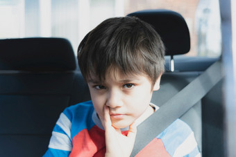 肖像年轻的男孩与无聊脸孩子伤心脸坐着的回来乘客座位与安全带不开心孩子看出被宠坏的孩子们概念