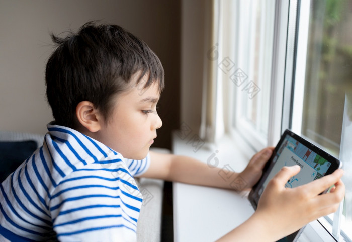 电影肖像年轻的男孩玩游戏平板电脑坐着沙发与光闪亮的从窗口孩子玩游戏互联网孩子做家庭作业在线首页