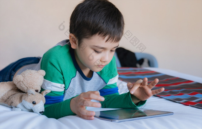 电影肖像孩子玩游戏在线互联网与朋友床上房间年轻的男孩使用平板电脑打字聊天晚上童年坐着床上放松首页周末