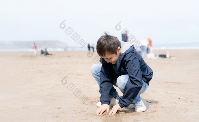 肖像快乐年轻的男孩玩和挖掘沙子的海滩阳光明媚的一天夏天孩子有有趣的与建筑沙子城堡热带海滩与模糊的背景人走的海
