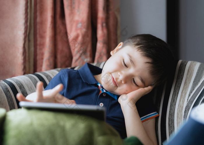 电影肖像年轻的男孩玩游戏平板电脑坐着沙发与光闪亮的从窗口孩子玩游戏在线互联网首页孩子会说话的视频调用与朋友首页