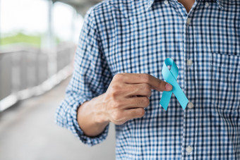 11月前列腺癌癌症意识月男人。蓝色的衬衫与手持有蓝色的丝带为支持人生活和疾病医疗保健国际但父亲和世界癌症一天概念