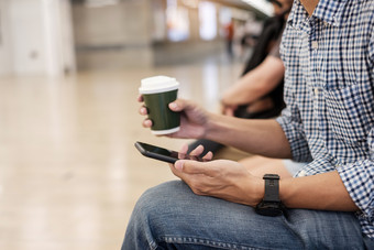 年轻的休闲商人坐着和使用智能手机之间的喝热咖啡业务生活方式技术和社会媒体网络概念