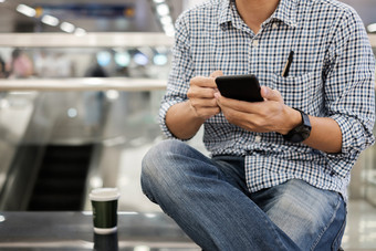 年轻的休闲商人坐着和使用智能手机之间的喝热咖啡业务生活方式技术和社会媒体网络概念
