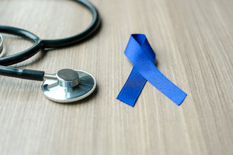 结肠癌症意识黑暗蓝色的丝带与听诊器为支持人生活和疾病医疗保健和世界癌症一天概念