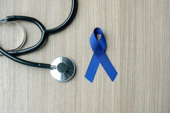 结肠癌症意识黑暗蓝色的丝带与听诊器为支持人生活和疾病医疗保健和世界癌症一天概念