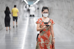 年轻的亚洲女孩穿外科手术脸面具保护冠状病毒变形快乐旅游女人使用智能手机在走地铁站新正常的和生活后新冠病毒流感大流行