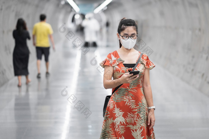 年轻的亚洲女孩穿外科手术脸面具保护冠状病毒变形快乐旅游女人使用智能手机在走地铁站新正常的和生活后新冠病毒流感大流行