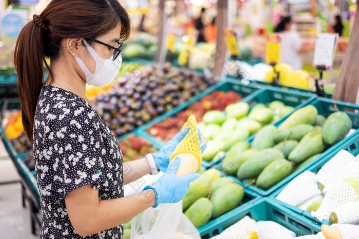 亚洲女人穿腈手套和持有成熟的芒果水果超市杂货店保护冠状病毒变形卫生新正常的和生活后新冠病毒流感大流行