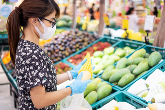 亚洲女人穿腈手套和持有成熟的芒果水果超市杂货店保护冠状病毒变形卫生新正常的和生活后新冠病毒流感大流行