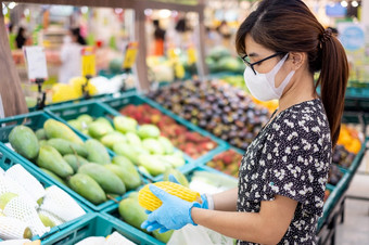 亚洲女人穿腈手套和持有成熟的芒果水果超市杂货店保护冠状病毒变形卫生新正常的和生活后新冠病毒流感大流行