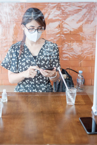 亚洲女人使用<strong>智能</strong>手机在<strong>餐厅</strong>时间<strong>餐厅</strong>与分离盾塑料分区保护冠状病毒变形社会距离新正常的和生活后新冠病毒流感大流行