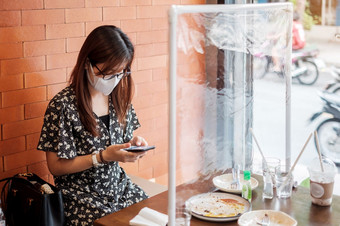 亚洲女人使用智能手机在<strong>餐厅</strong>时间<strong>餐厅</strong>与分离盾塑料分区保护冠状病毒变形社会距离新正常的和生活后新冠病毒流感大流行