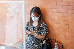 亚洲女人使用智能手机在餐厅时间餐厅与分离盾塑料分区保护冠状病毒变形社会距离新正常的和生活后新冠病毒流感大流行