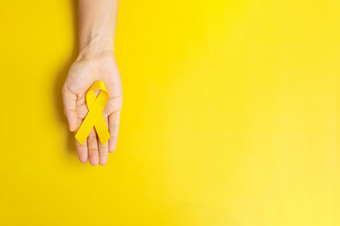 手持有黄色的丝带黄色的背景为支持人生活和疾病自杀<strong>预防</strong>一天肉瘤<strong>癌症</strong>和童年<strong>癌症</strong>意识月概念
