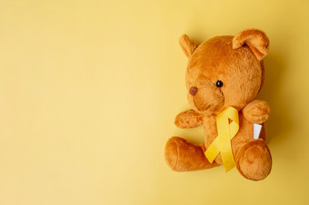 黄色的丝带与熊娃娃黄色的颜色背景为支持孩子生活和疾病9月童年癌症意识月和世界癌症一天概念