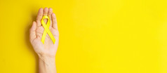 手持有黄色的丝带黄色的背景为支持人生活和疾病9月自杀预防一天童年癌症意识月和世界癌症一天概念