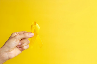 手显示黄色的丝带黄色的背景为支持人生活和疾病9月<strong>自杀预防</strong>一天童年癌症意识月和<strong>世界</strong>癌症一天概念