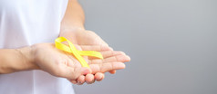 手持有黄色的丝带为支持人生活和疾病9月自杀预防一天童年肉瘤和骨癌症意识月概念