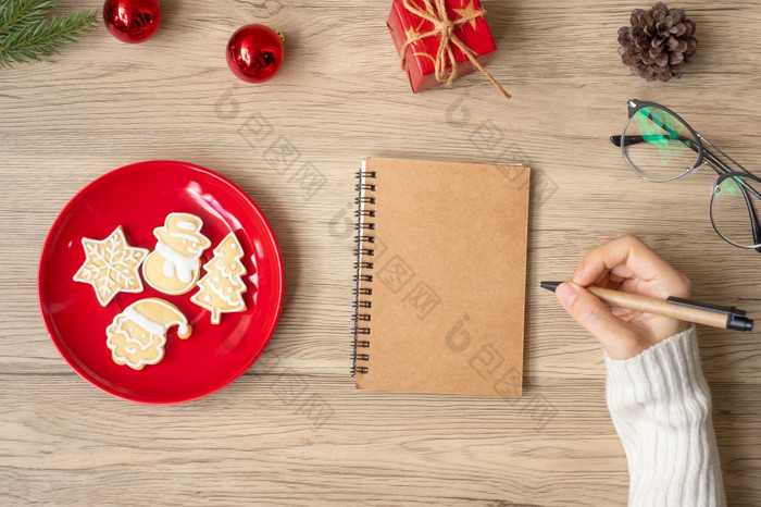女人手写作笔记本与圣诞节饼干表格圣诞节快乐新一年目标决议列表策略和计划概念