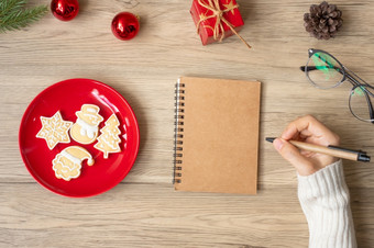 女人手写作笔记本与<strong>圣诞节</strong>饼干表格<strong>圣诞节快乐</strong>新一年目标决议列表策略和计划概念