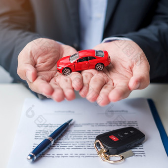 商人手持有红色的车玩具与车辆无钥匙笔和合同文档买和出售保险租赁和合同协议概念