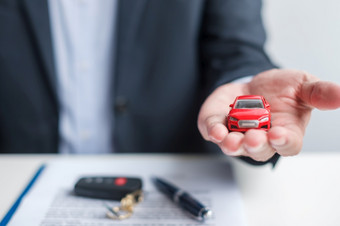 商人手持有红色的车玩具与车辆无钥匙笔和合同文档买和出售保险租赁和合同协议概念