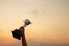 胜利概念与手持有奖杯的日落天空背景