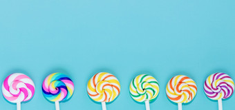 美味的棒棒糖蓝色的柔和的纸颜色背景集现实的螺旋条纹色彩斑斓的棒棒糖白色塑料棒夏天和流行艺术概念前视图