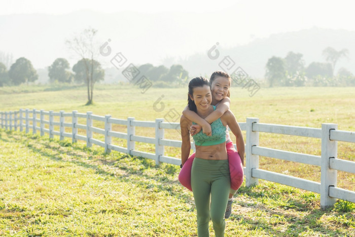 可爱的年轻的女儿小猪回来骑与妈妈。她的支出时间农村快乐家庭草地夏天自然户外体育和健身锻炼学习为孩子发展