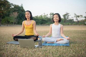 妈妈。和女儿做瑜伽女人和孩子培训的公园户外体育健康的体育运动生活方式看瑜伽练习在线视频教程和冥想实践在工作出