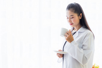 肖像亚洲年轻的女医<strong>生吃</strong>咖啡从杯和听诊器与医院背景