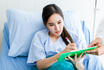 亚洲年轻的女病人签名为同意形式床上医生的房间医院背景