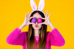 复活节假期概念快乐微笑亚洲年轻的女人穿兔子耳朵和持有色彩斑斓的复活节蛋前面她的眼睛串孤立的黄色的空白复制空间工作室背景