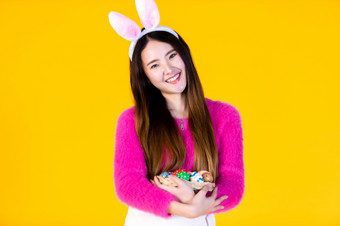 复活节假期概念快乐亚洲年轻的女人穿<strong>兔子</strong>耳朵手持有篮子与色彩斑斓的复活节鸡蛋和的一边<strong>眼睛</strong>看相机孤立的黄色的空白复制空间工作室