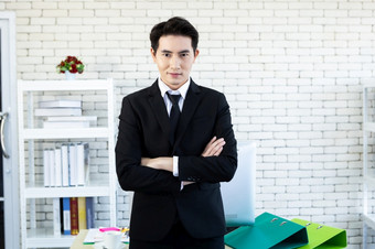 肖像快乐的成熟的亚洲年轻的商人穿业务西装男人。蓝色的夹克和蓝色的衬衫看的窗口的办公室房间背景