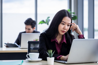 心烦意乱深思熟虑的年轻的亚洲业务女人压力的工作场所工作与移动PC电脑办公室工作人员是不快乐与工作的同事们后面的办公室