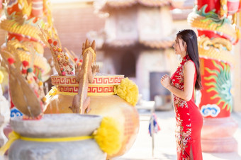 美丽的亚洲年轻的女人穿红色的<strong>传统</strong>的中国人<strong>旗袍</strong>装饰站为祈祷佛雕像为中国人新一年节日中国人神社泰国